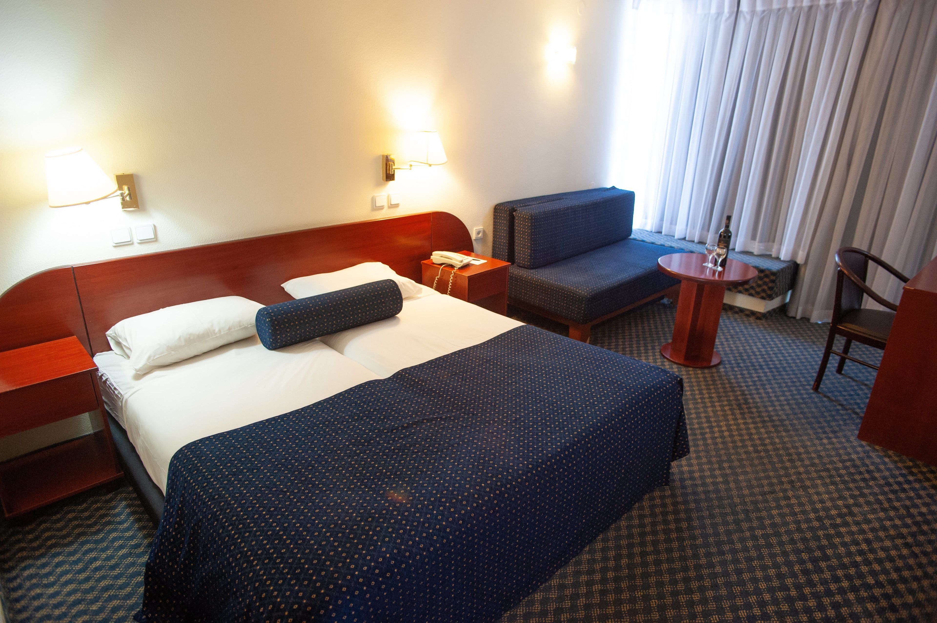 Habitación de hotel con una cama grande, un escritorio, una silla y una mesita con una botella y un vaso.