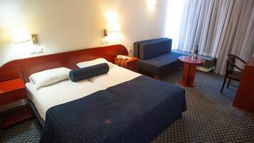A hotel room with a large bed, a desk, a chair, and a small table with a bottle and glass.