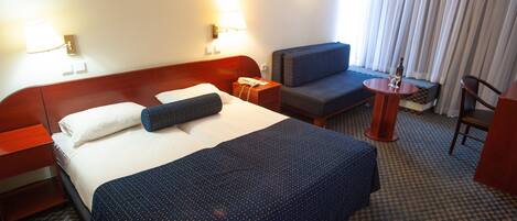 Habitación de hotel con una cama grande, un escritorio, una silla y una mesita con una botella y un vaso.