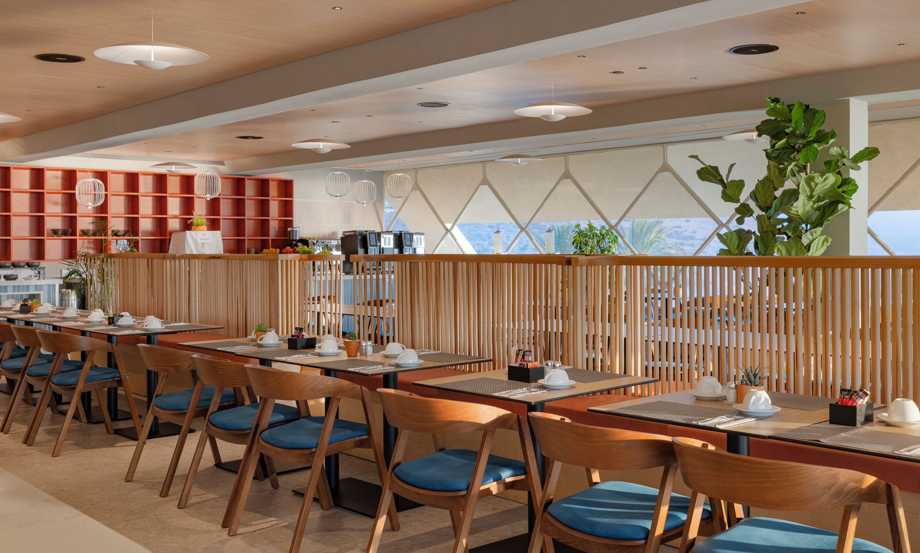 A modern restaurant with wooden furniture, a high ceiling, and a view of the mountains.
