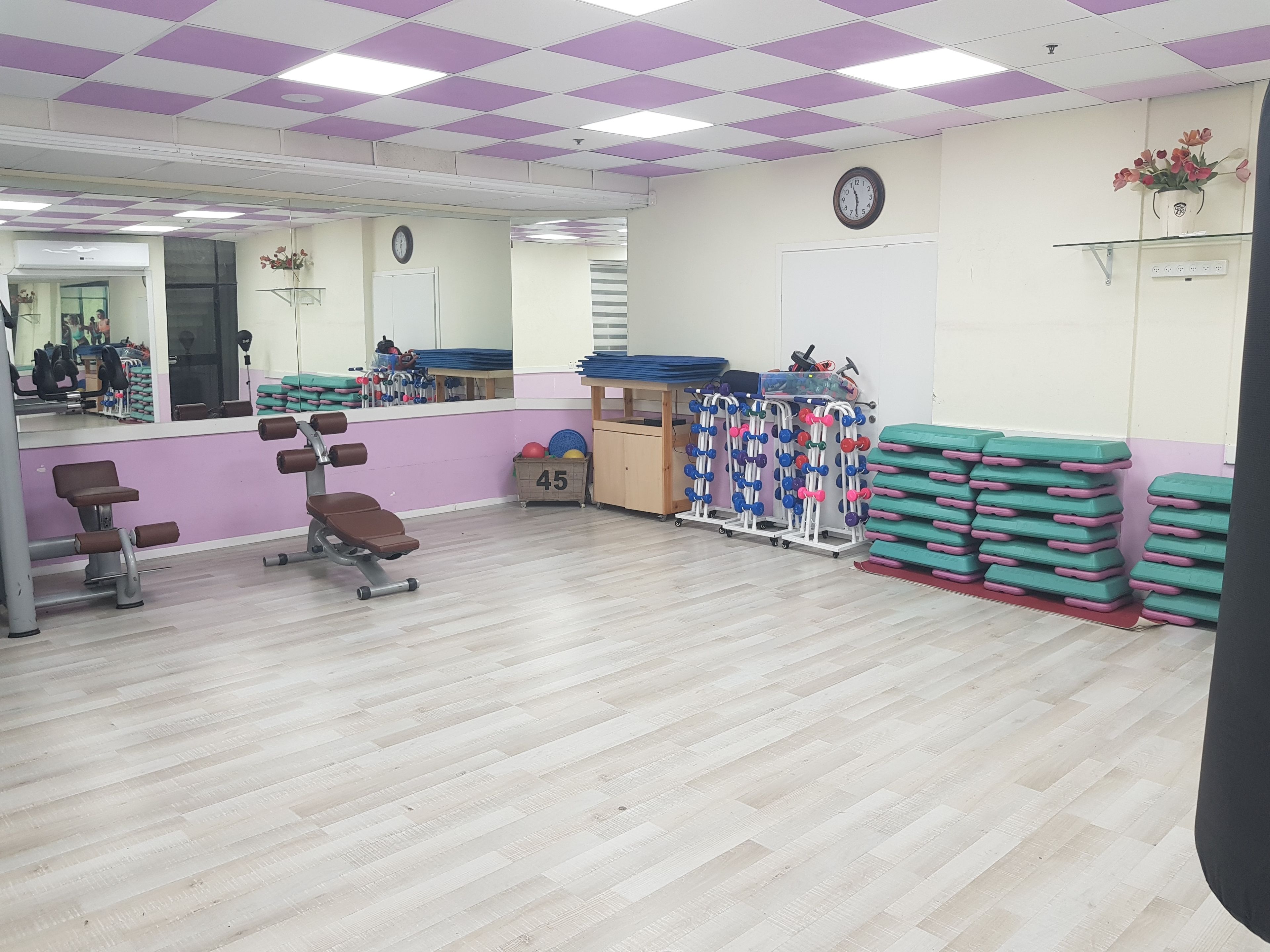 Une salle de sport équipée de matériel d’exercice, avec un miroir et une horloge au mur.