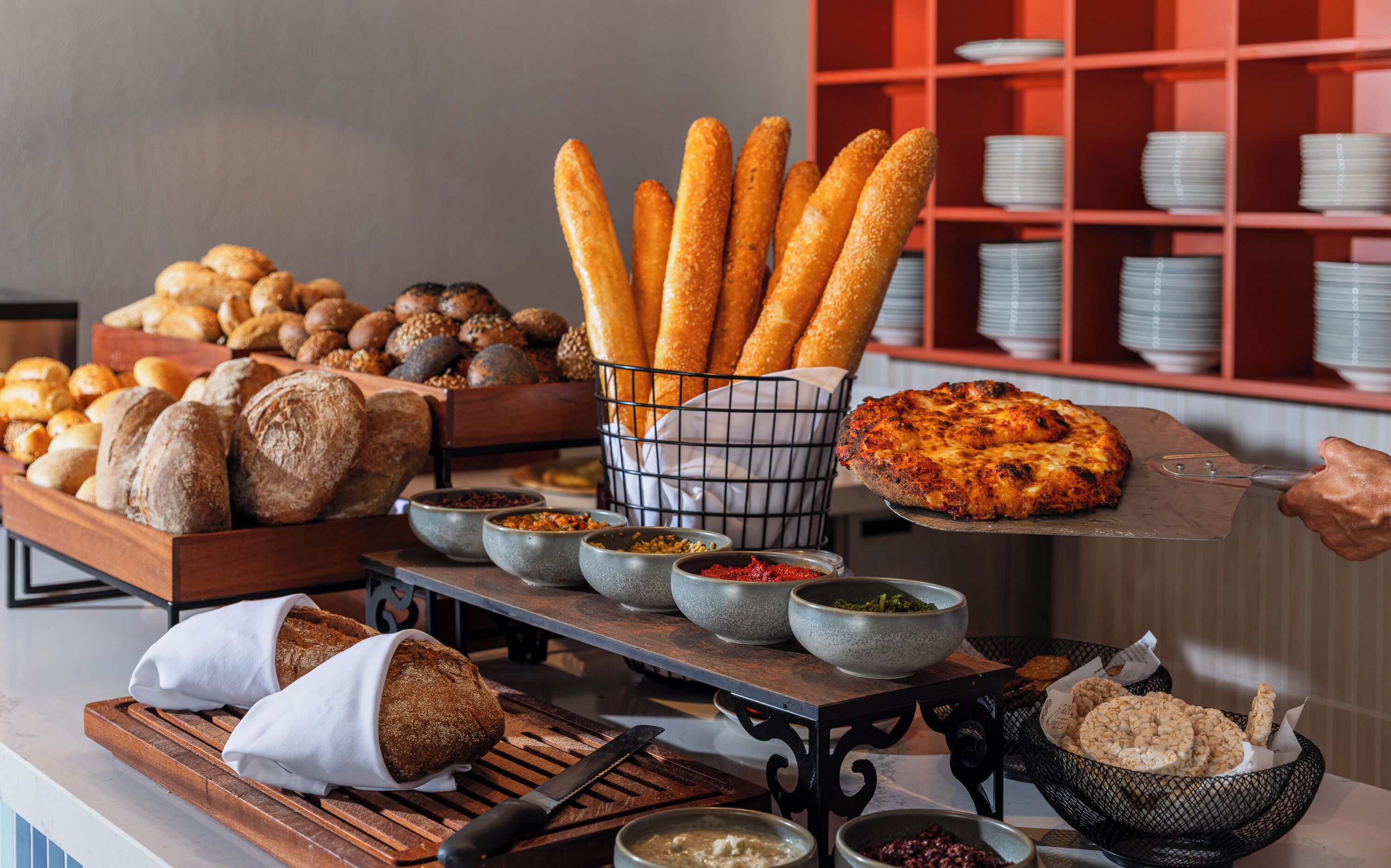 Une table de buffet proposant divers types de pains, de petits pains et une pizza.