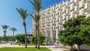 Un edificio moderno con fachada geométrica, rodeado de palmeras y vegetación.