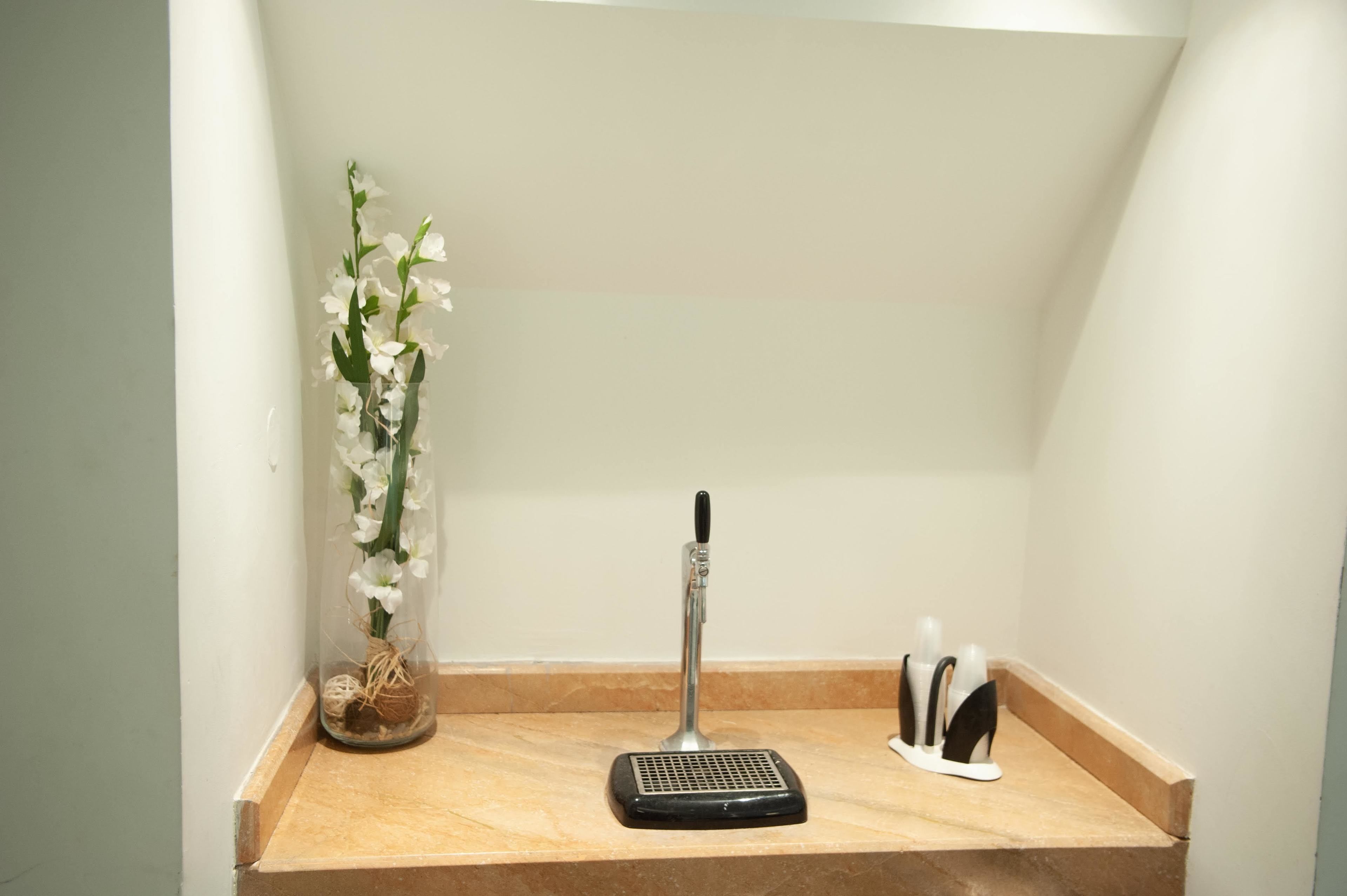 A small, enclosed space with a vacuum cleaner, a vase with white flowers, and a knife block.