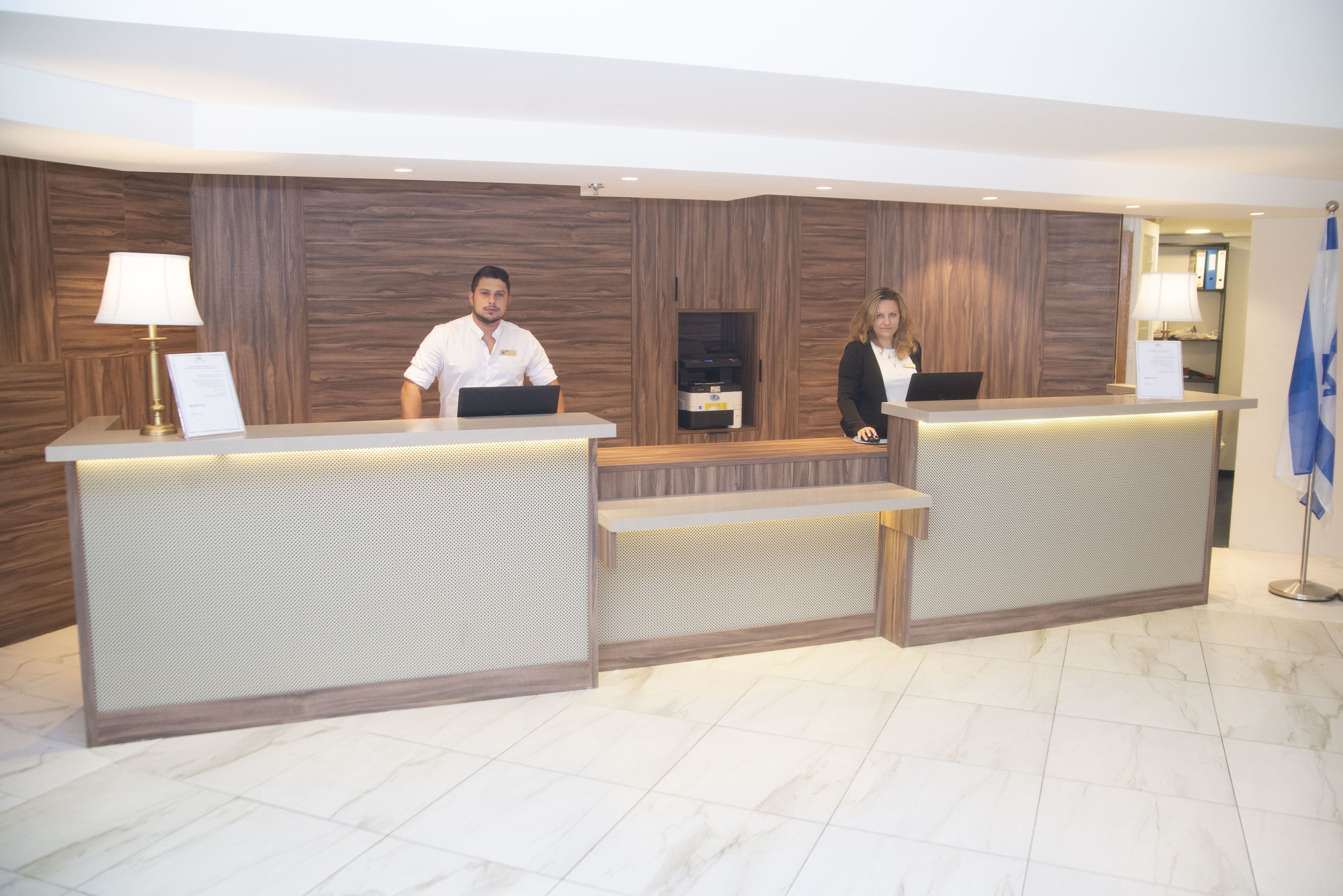 A reception desk with two staff members, a wooden wall, and a flag.