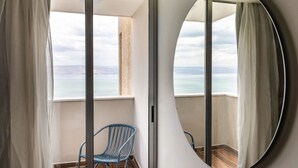 Un balcón con vista al mar, una silla azul y un espejo redondo.