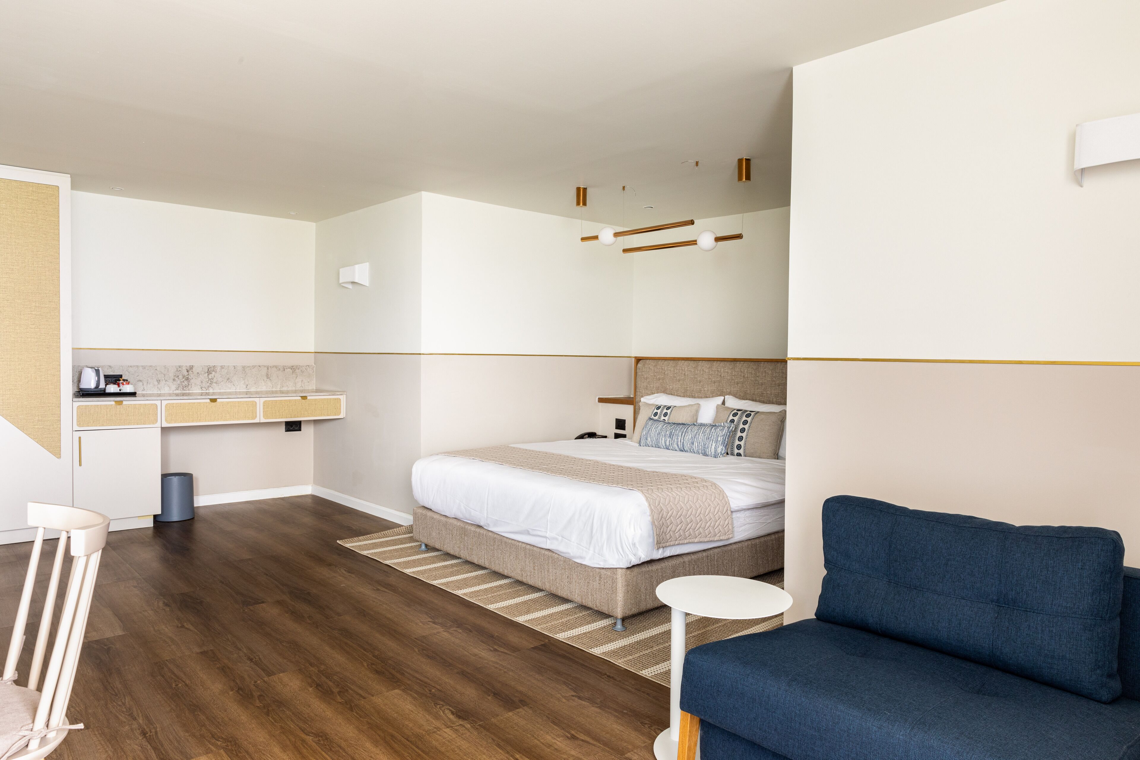 Une chambre d’hôtel moderne avec un grand lit, un canapé bleu, une petite table et un coin cuisine.