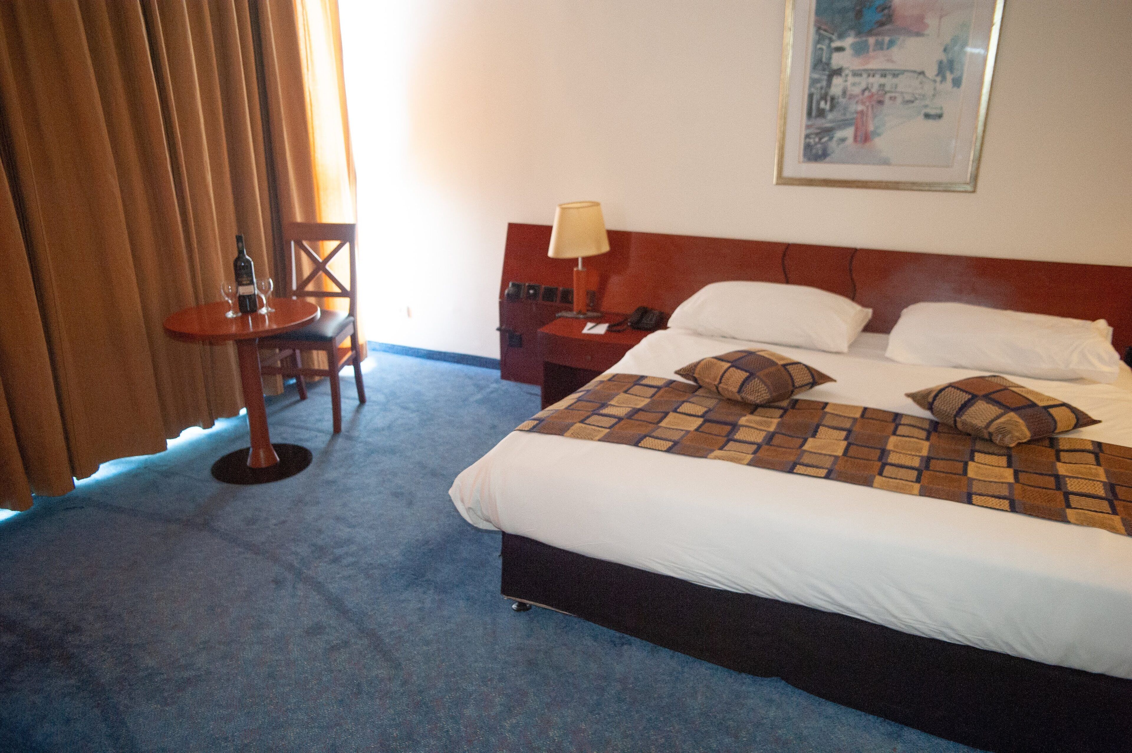 Ein Hotelzimmer mit einem Bett, einem Nachttisch, einer Lampe, einem Sessel und einem Tisch mit Flasche und Gläsern.