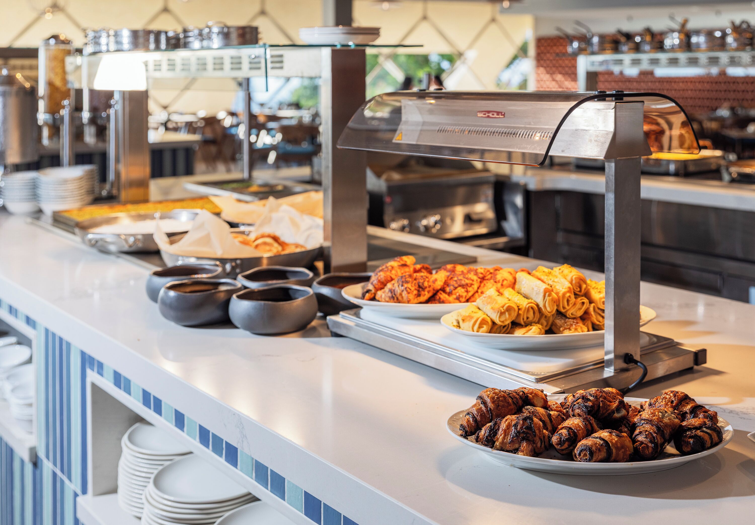 Un buffet proposant une variété de plats, notamment des viandes grillées et des pâtisseries, disposés sur un comptoir dont le mur arrière est recouvert de carreaux.