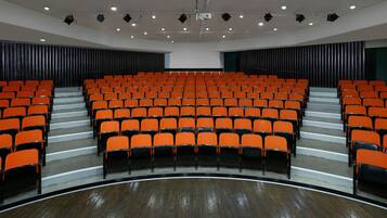 A theater with rows of orange seats, a stage, and a large screen.