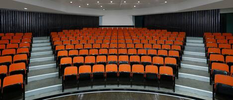 A theater with rows of orange seats, a stage, and a large screen.
