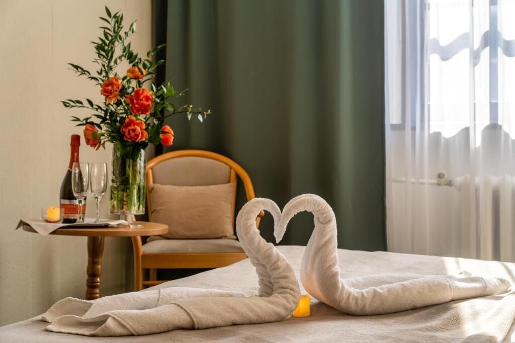 Una habitación de hotel con cama, una silla, una mesa con un florero y una botella de vino.