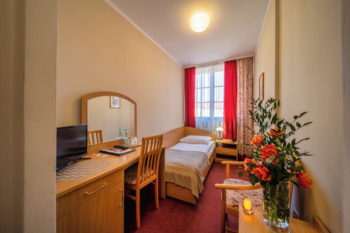 A hotel room with a bed, desk, chair, TV, and a vase of flowers.