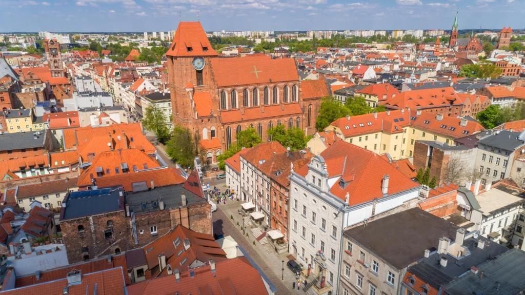 Egy városkép, amelyen egy feltűnő, vörös tetővel rendelkező templom és a környező épületek láthatók.
