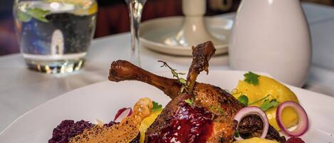 A plate of food with a lamb shank, potatoes, and berries, accompanied by a glass of wine and a candle.