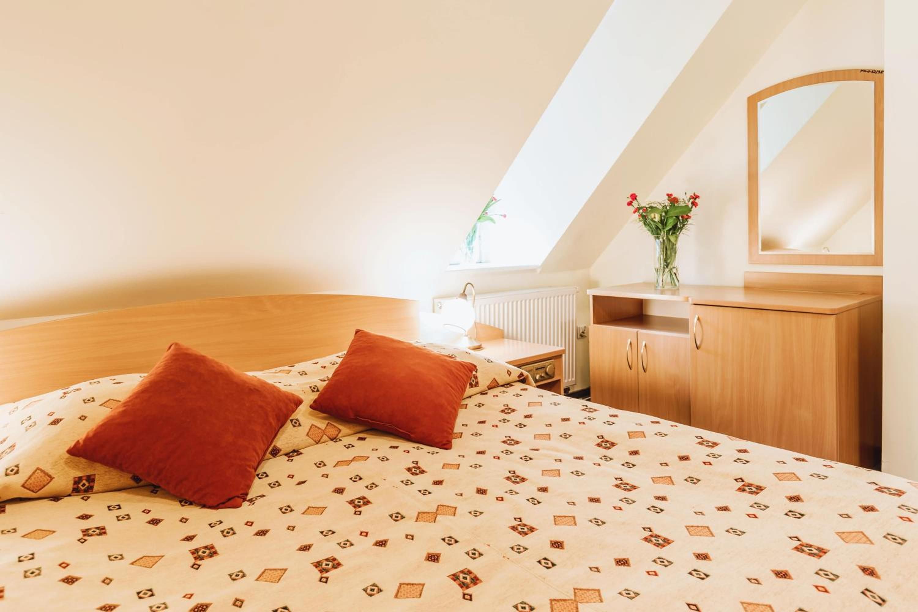 A bedroom with a sloped ceiling, a bed with patterned bedding, a nightstand, a dresser, and a mirror.
