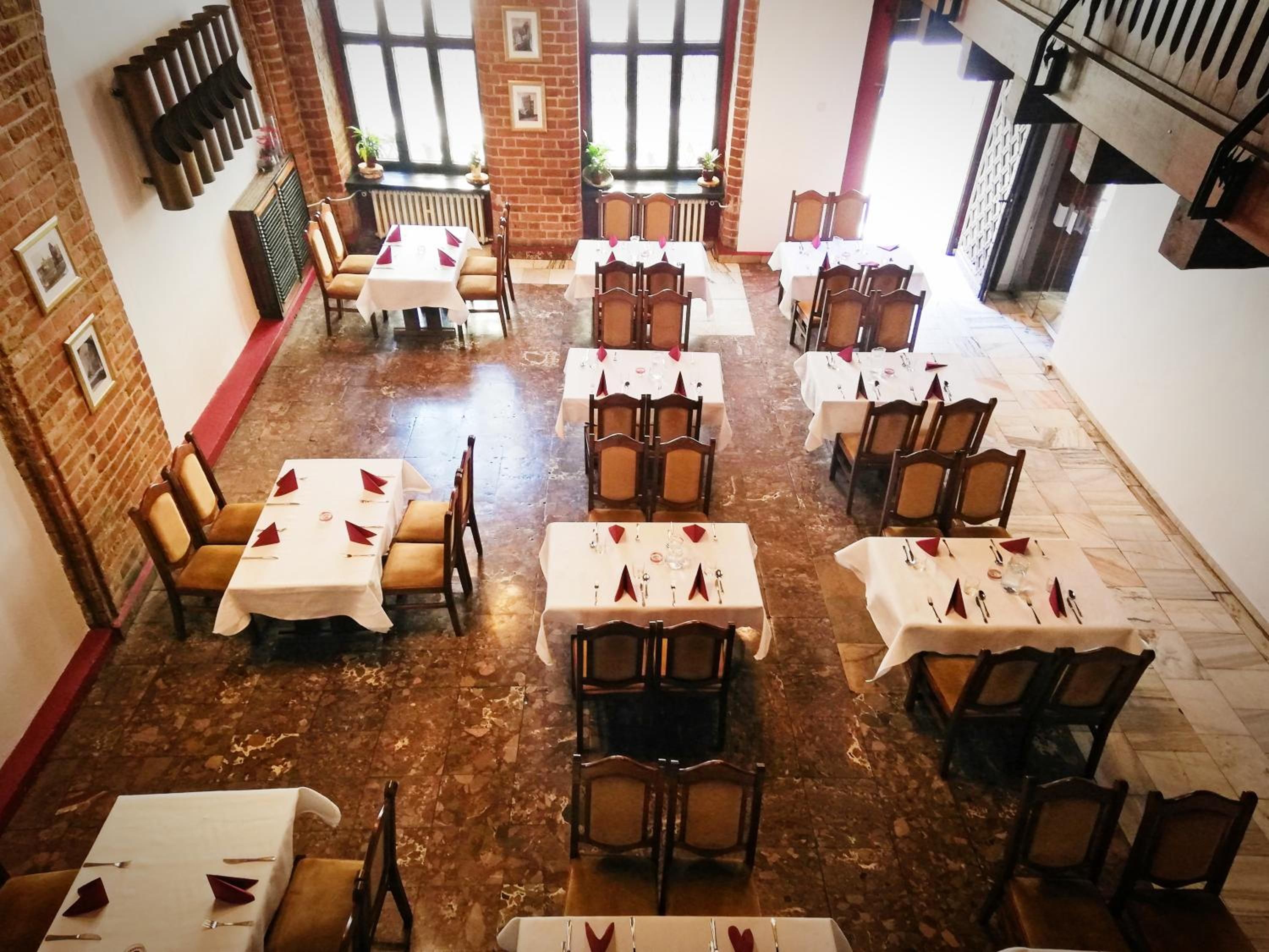 A dining area with multiple tables and chairs, arranged in a spacious layout with brick walls and large windows.