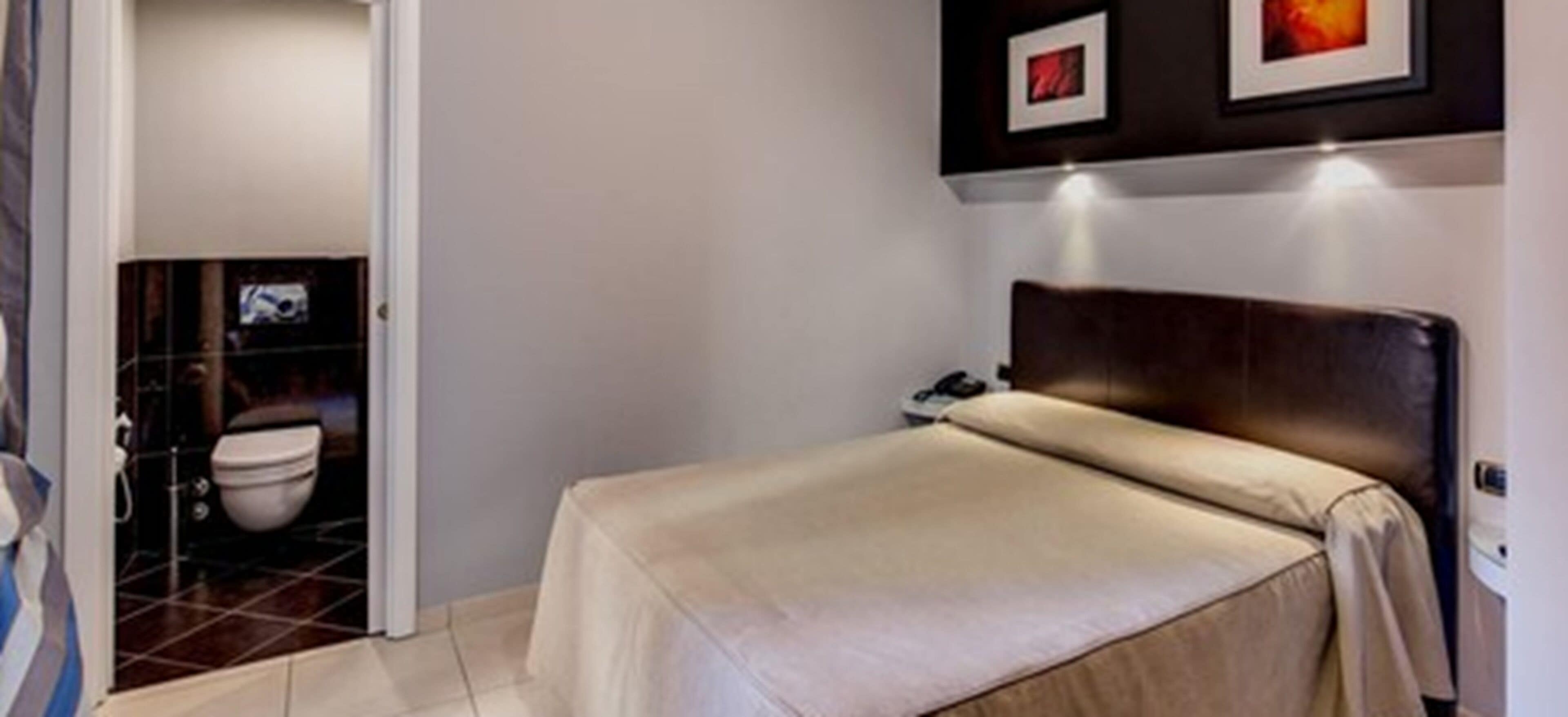 Une chambre à coucher comprenant un lit, une table de chevet, une commode et un téléviseur fixé au mur.