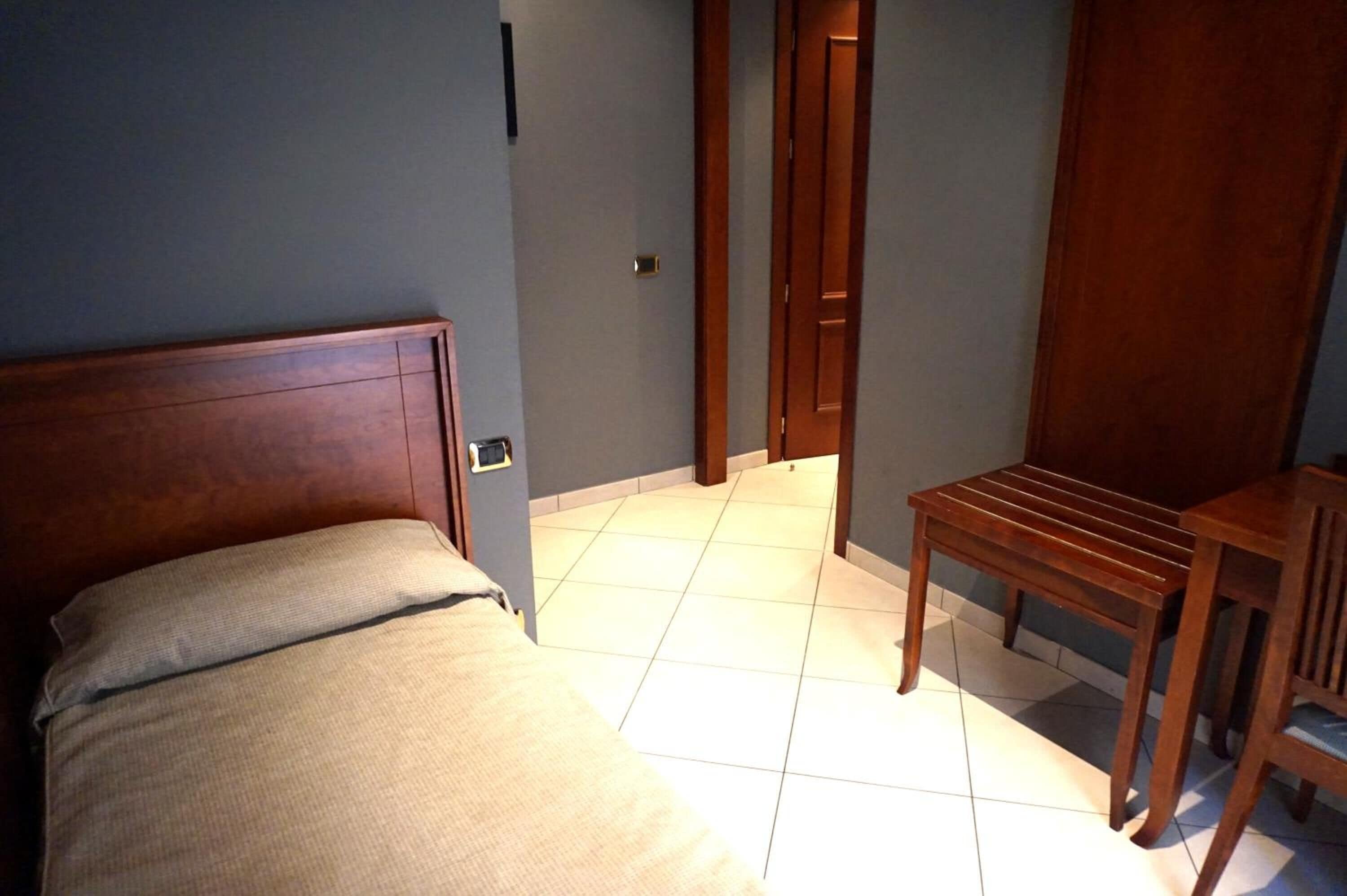 A bedroom with a wooden bed, a small wooden table, and a door leading to another room.