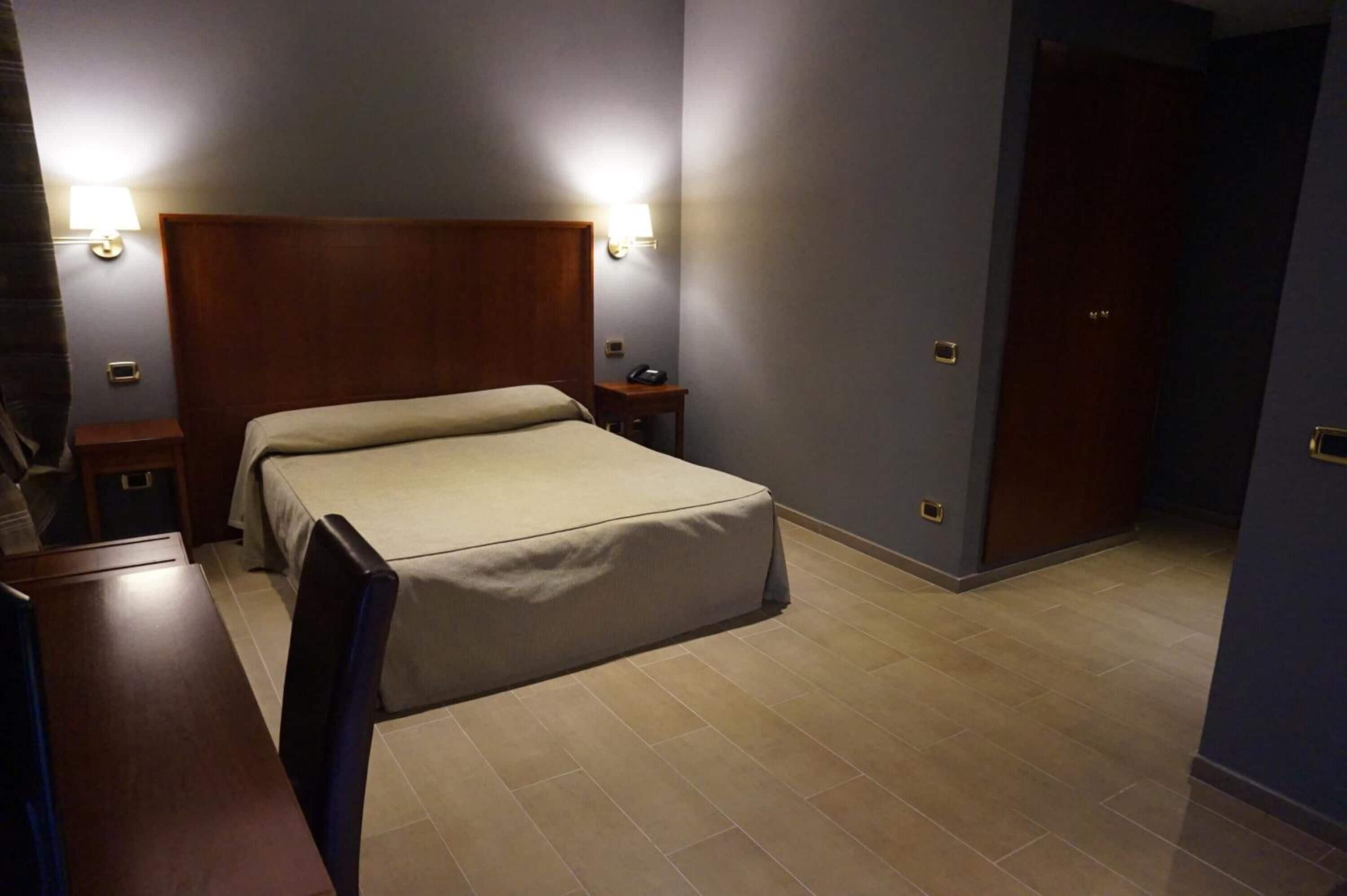 A hotel room with a bed, bedside tables, and a door.