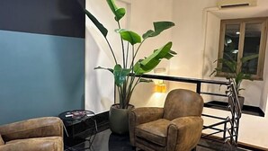 Un vestíbulo moderno con pared azul y negra, una planta grande en maceta, un sillón marrón y una mesita pequeña.