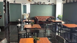 Un café moderno con mesas de madera y sillas negras, un sofá de cuero e iluminación colgante.