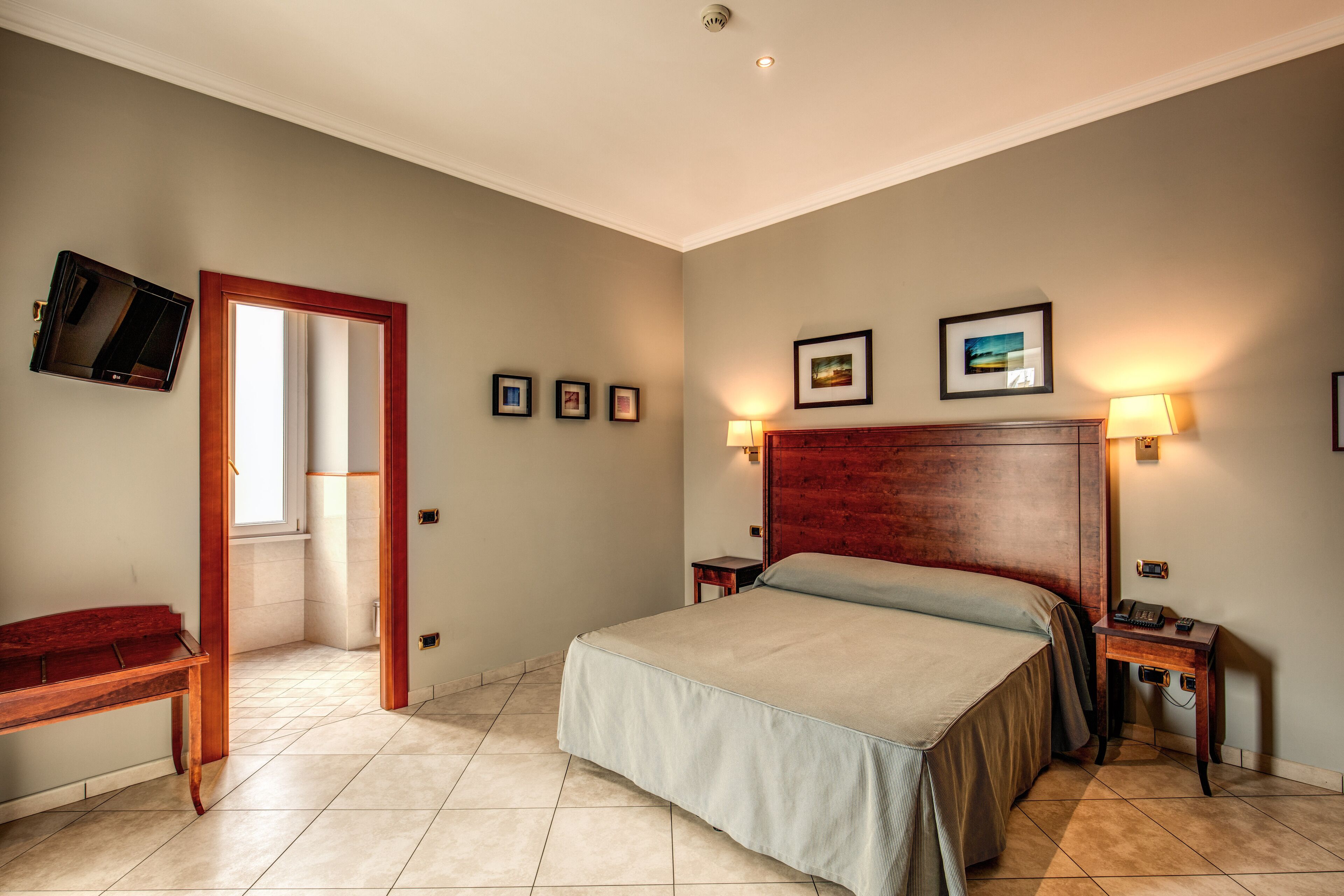 Quarto com cama, mesas de cabeceira, televisão e quadros nas paredes.