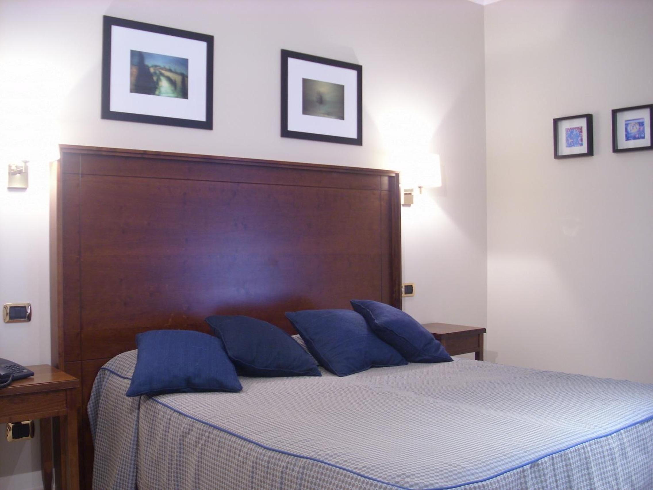 A bedroom with a large wooden headboard, a bed with a checkered bedspread, and two framed pictures on the wall.