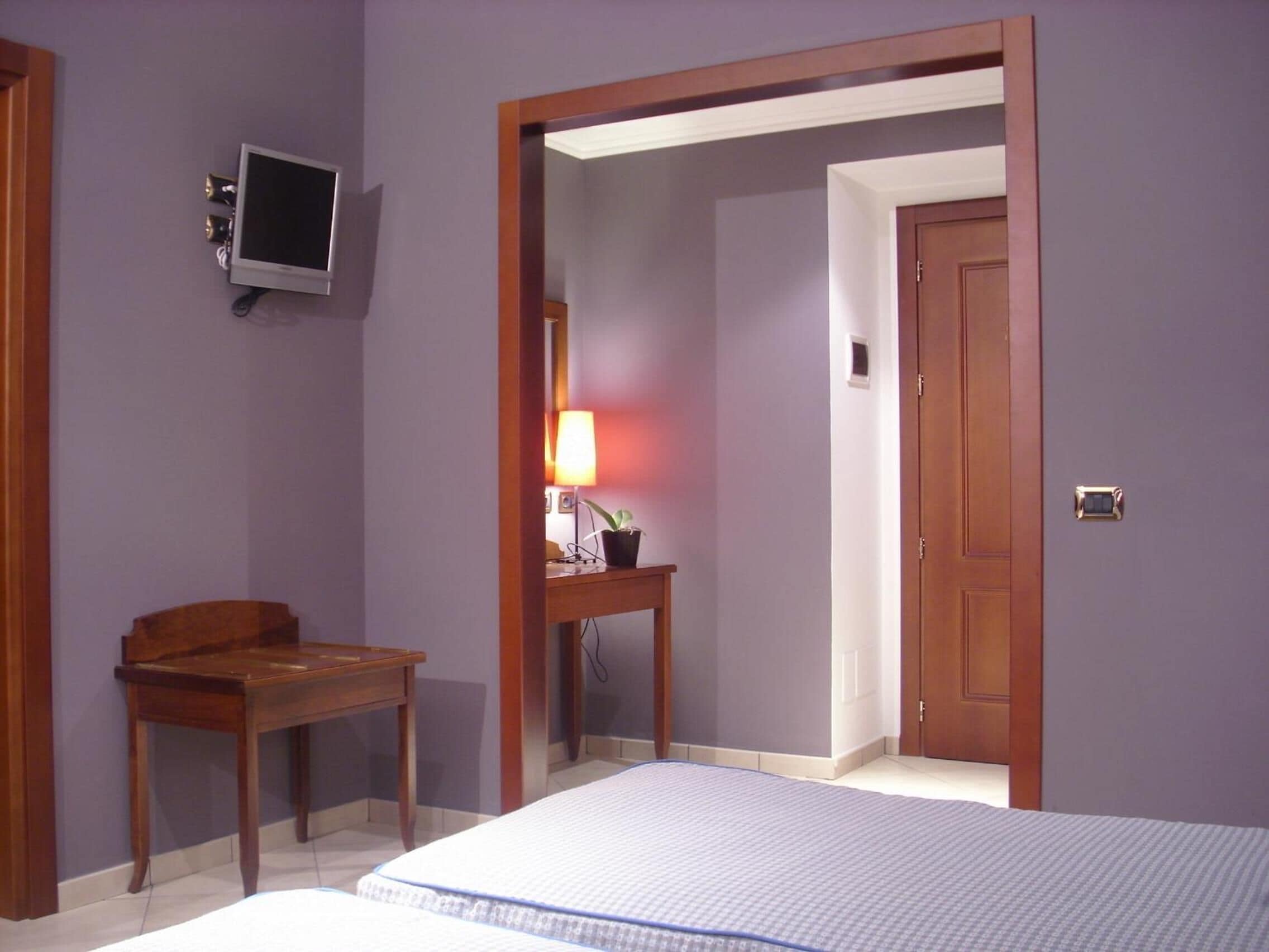 A bedroom with a bed, a desk, a lamp, a television, and a door.