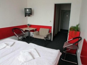 A hotel room with a bed, two chairs, a small table, and a television on the wall. - Slavia (Prague)