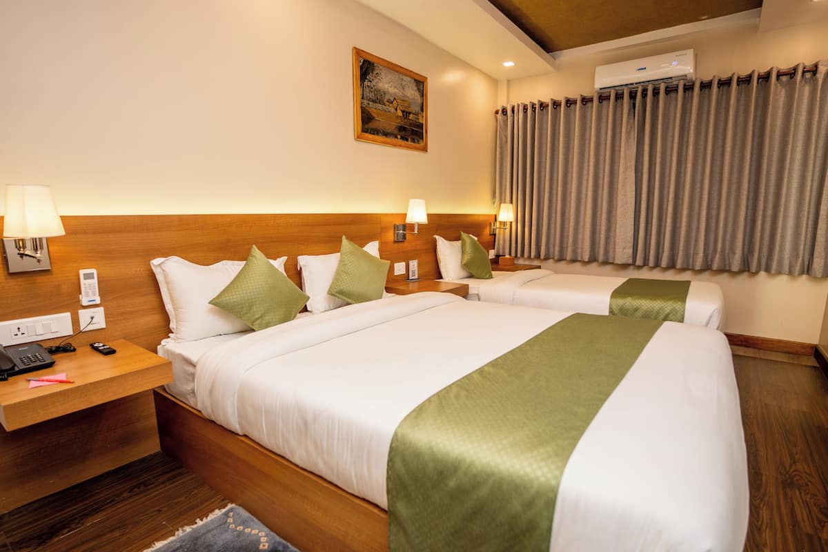 A hotel room with two beds, wooden headboards, bedside lamps, a painting on the wall, and a window with curtains.