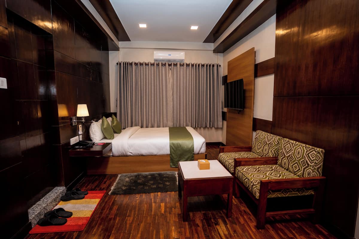 A hotel room with a bed, a sofa, a small table, a lamp, slippers, and a TV on the wall.