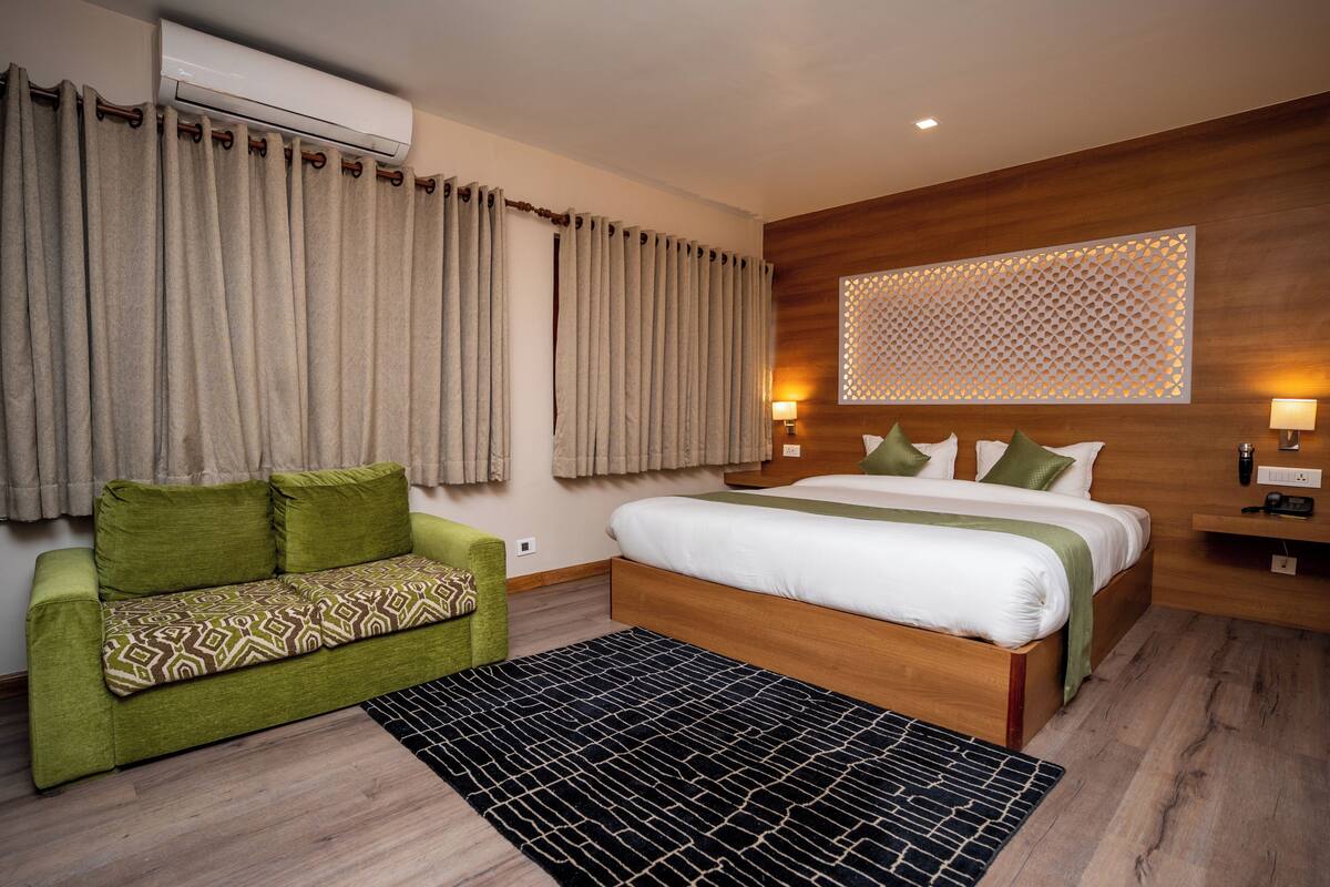 A modern hotel room with a wooden bed, green sofa, and a patterned rug.
