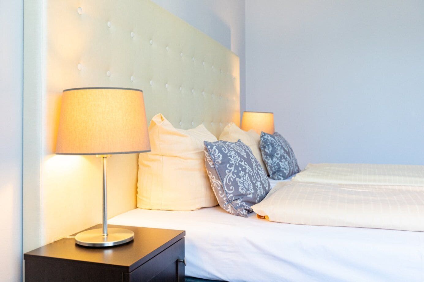 A neatly made bed with a tufted headboard, a bedside lamp, and patterned pillows.