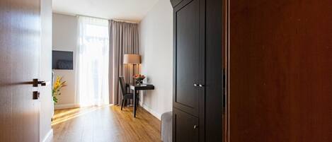 A hallway with wooden flooring, a dining area with a table and chairs, a lamp, and a large wardrobe.