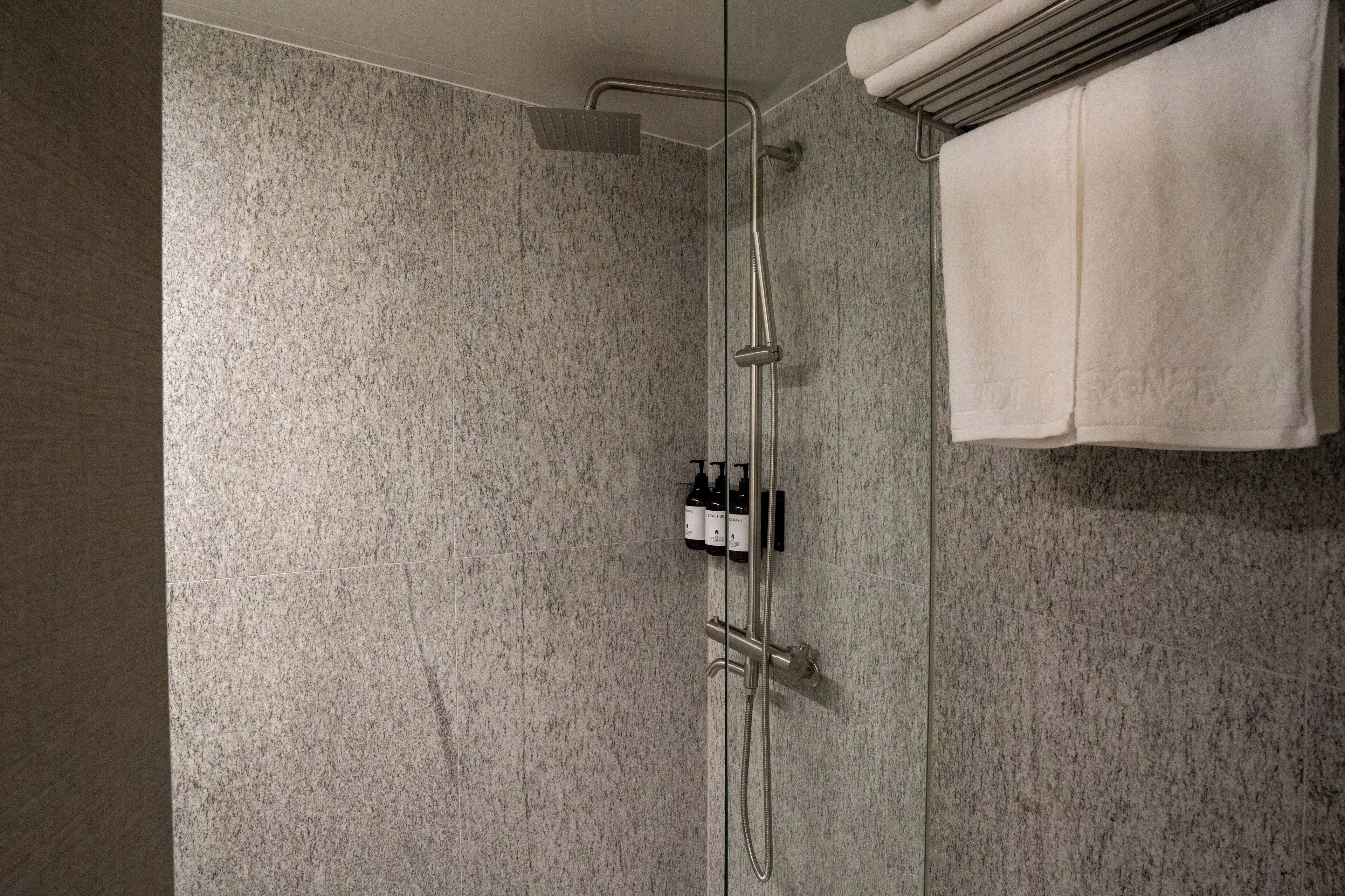 Une douche moderne avec un pare-douche en verre, un porte-serviettes et un ensemble de produits de toilette.