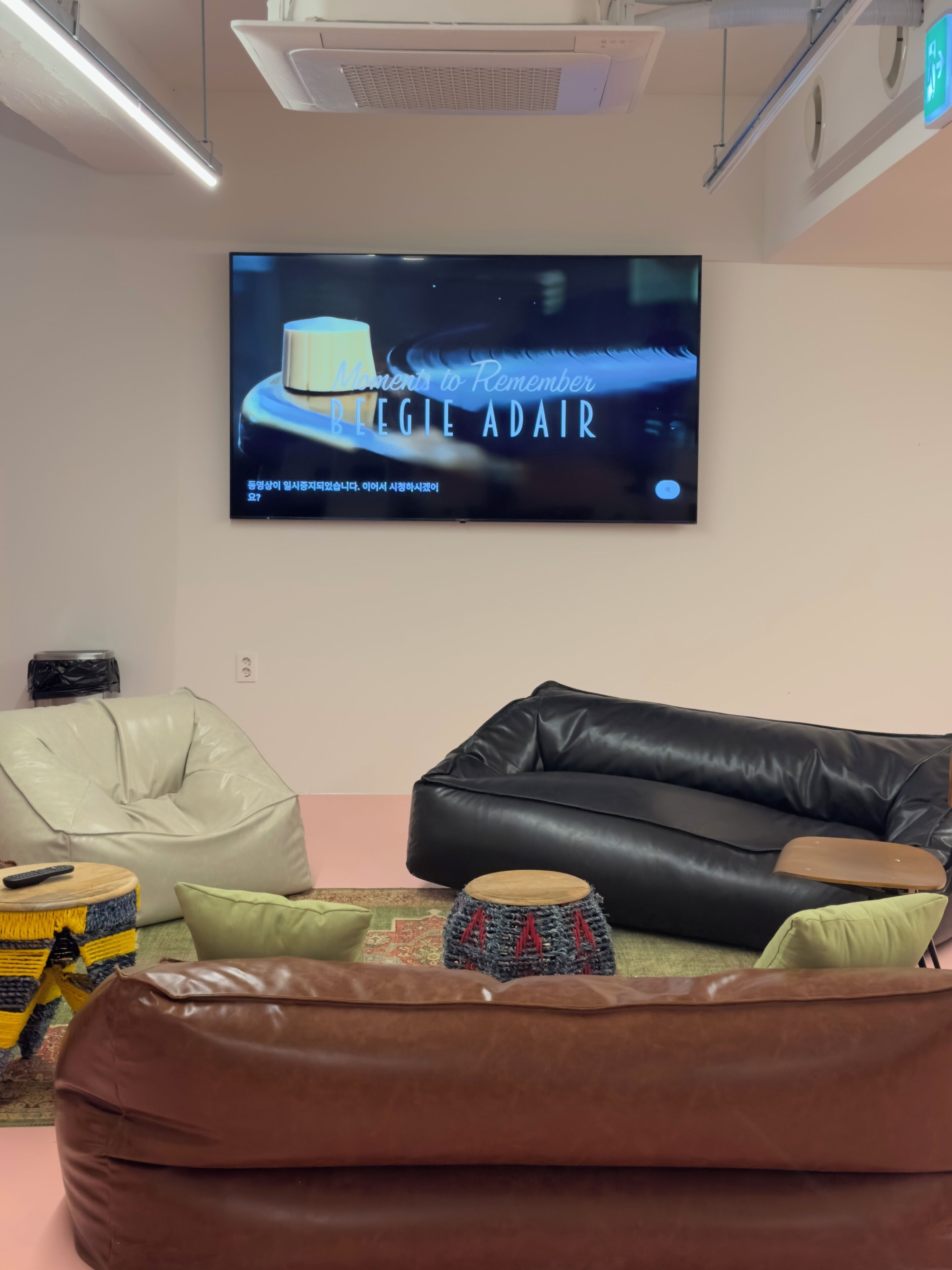 A living room with a flat-screen TV, a black leather sofa, a white bean bag, and a small drum.