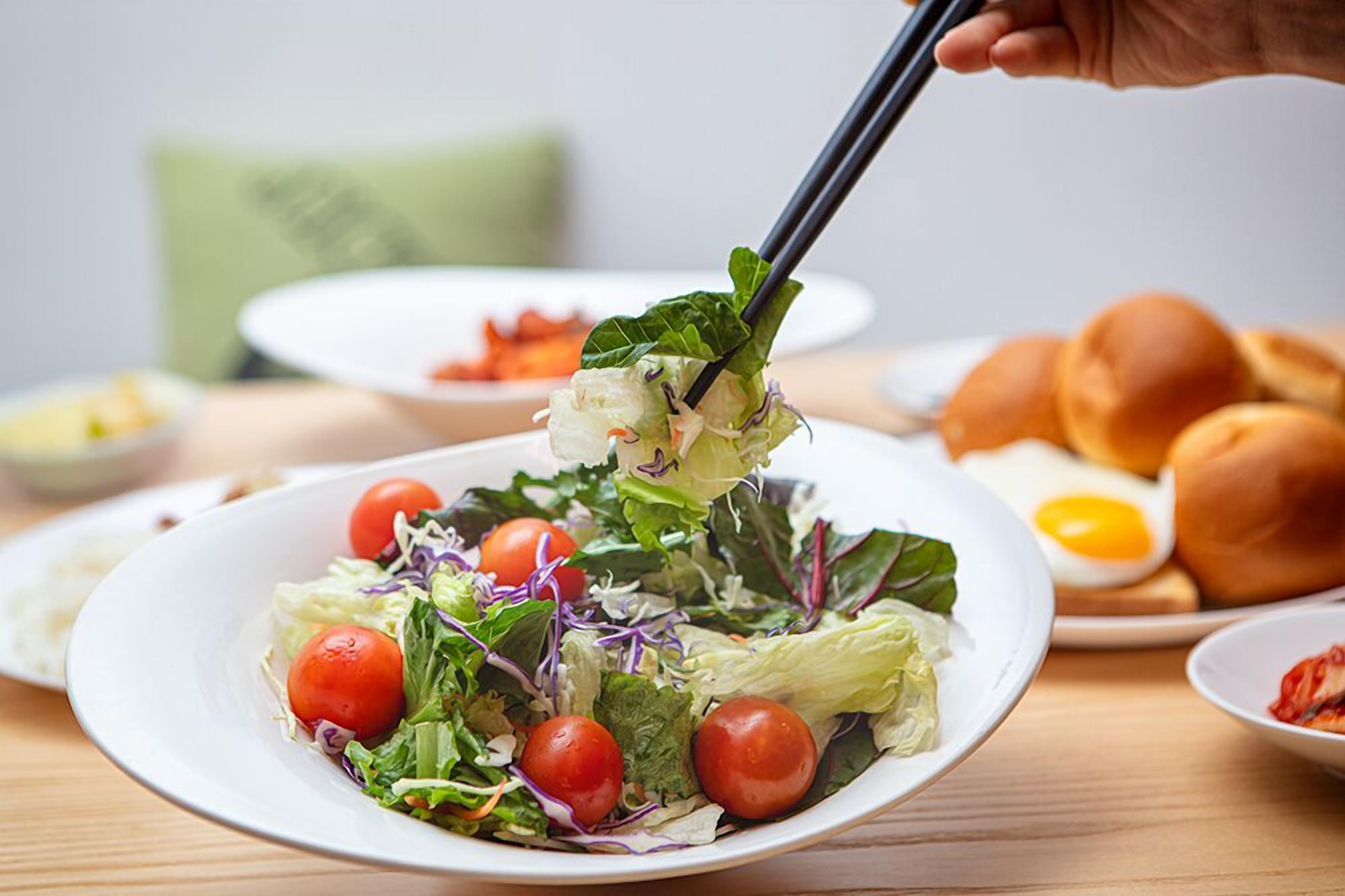 A plate of salad with lettuce and cherry tomatoes, a bowl of soup, and a plate of bread rolls.