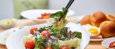 A plate of salad with lettuce and cherry tomatoes, a bowl of soup, and a plate of bread rolls.