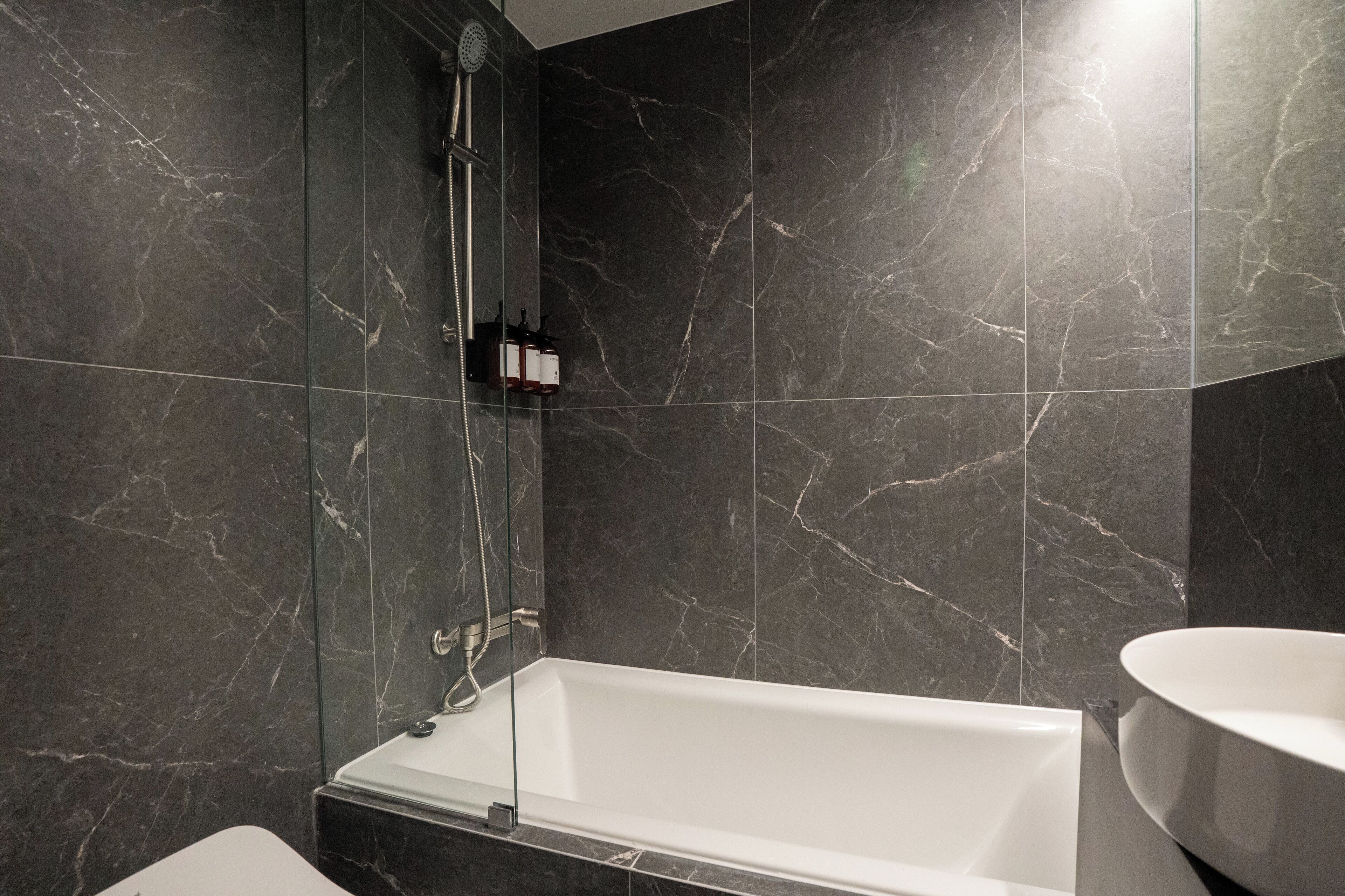 Un baño moderno con una bañera independiente, ducha con mampara de vidrio y pared revestida de mármol.