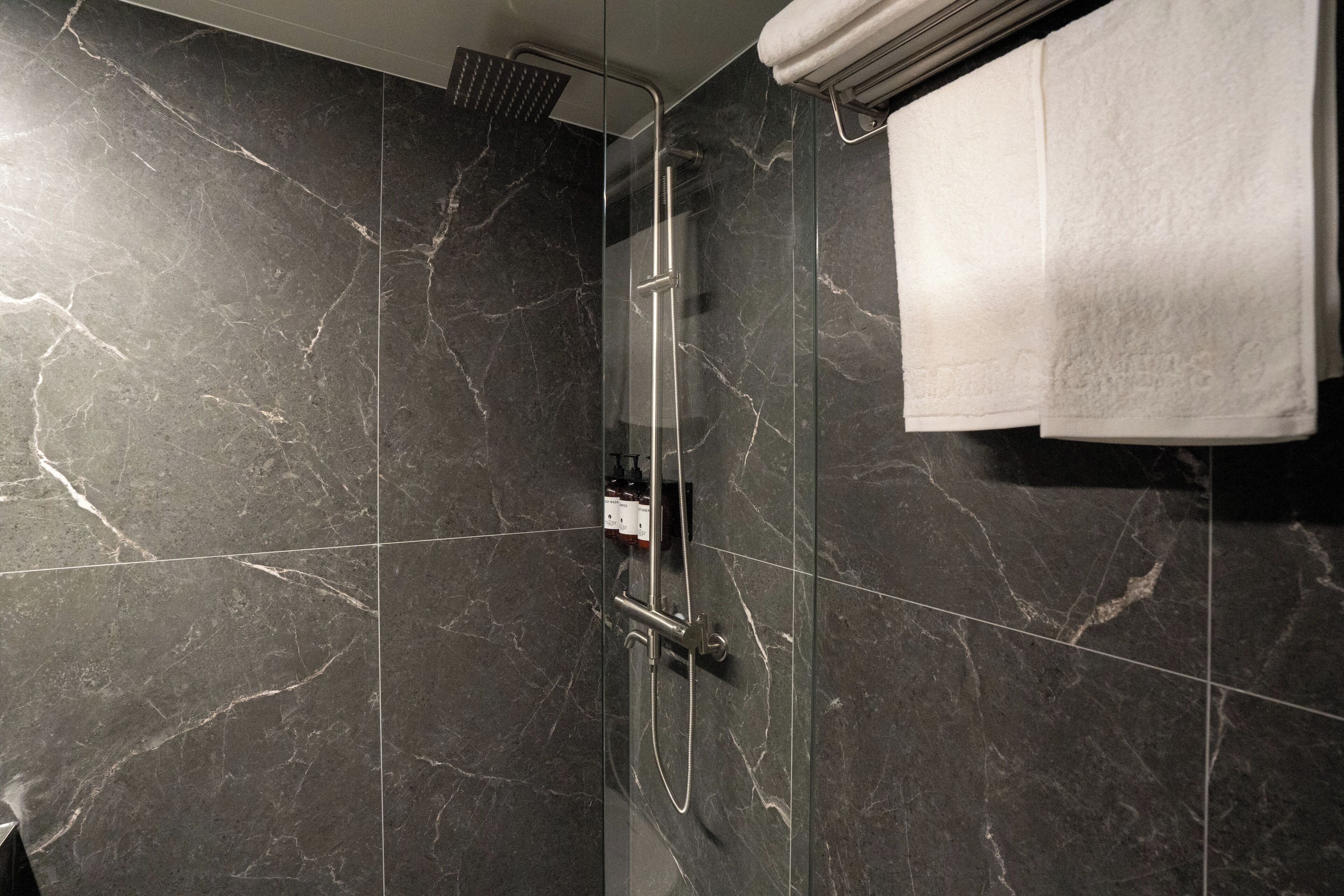 Un baño moderno con baldosas de mármol oscuro, ducha con mampara de vidrio y un perchero para toallas.