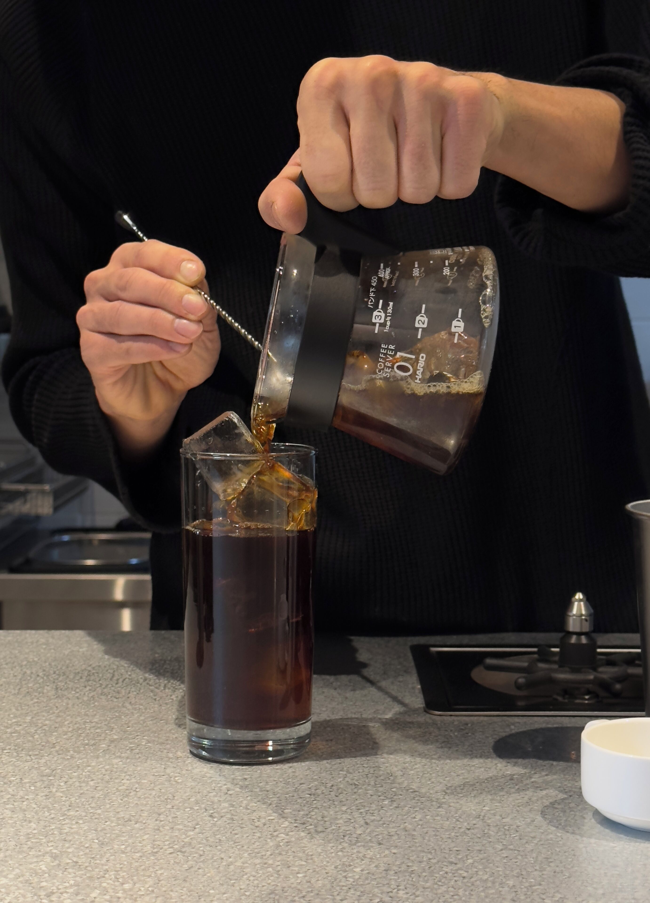 Iemand giet een drankje uit een maatbeker in een glas.