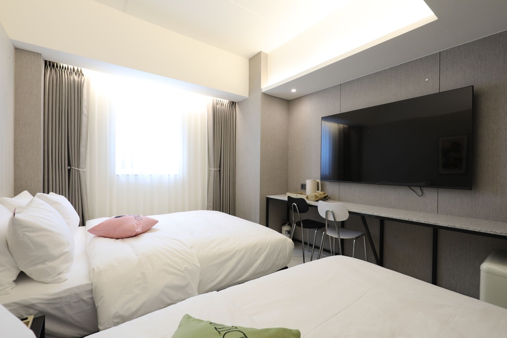 A hotel room with two beds, a TV mounted on the wall, and a desk with a chair.