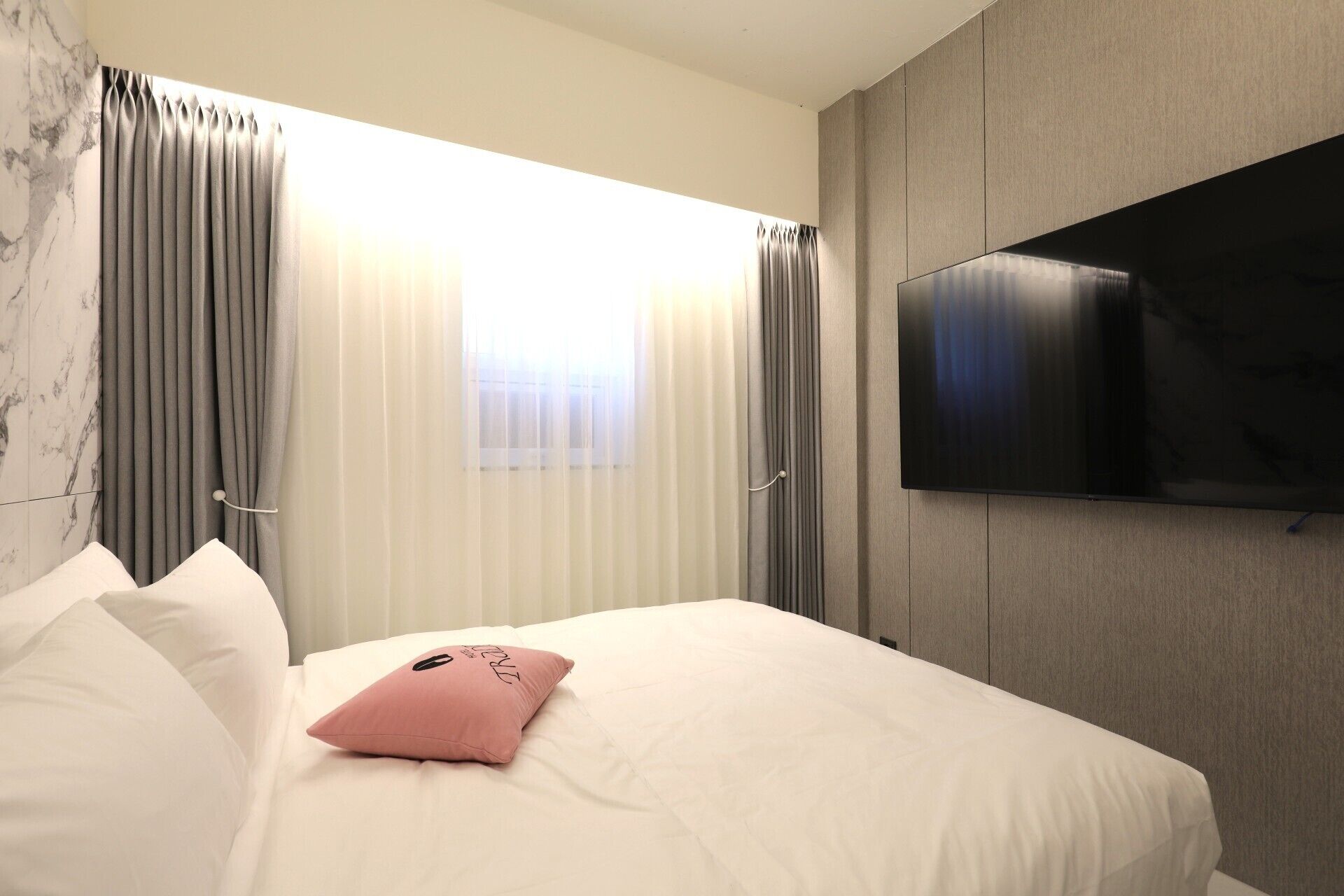 A hotel room with a bed, a TV mounted on the wall, and curtains on the windows.