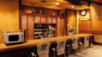 A hotel bar with a long counter, chairs, a microwave, and a clock on the wall.