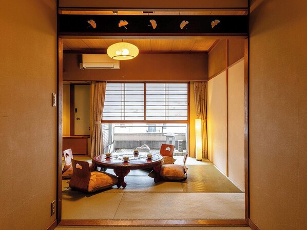 A traditional Japanese room with tatami flooring, a low table with cushions, and a sliding door leading to a balcony. - Ryokan Kuramoto (Osaka)