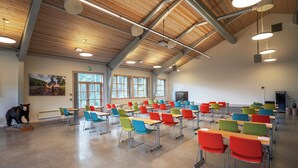A classroom with rows of desks and colorful chairs, wooden ceiling beams, and large windows. - Thon Hotel Bjørneparken (Flaa)