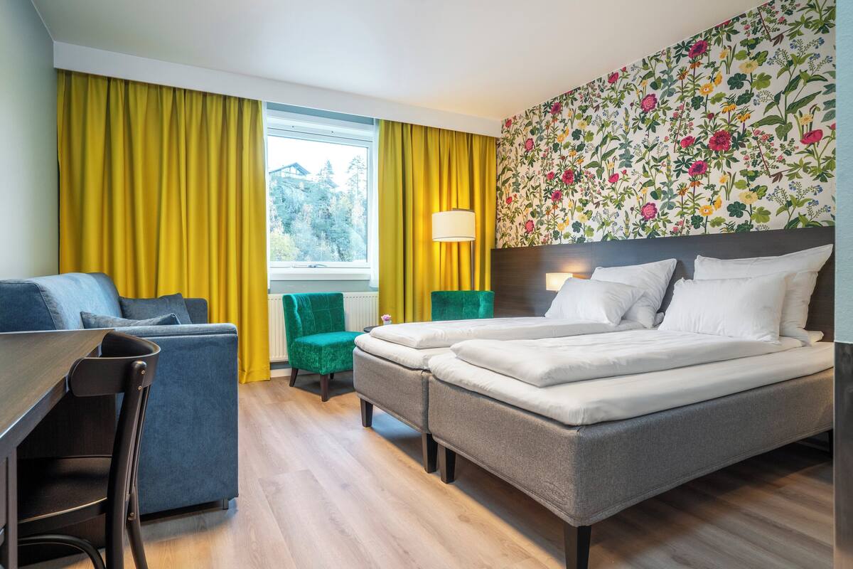 Quarto de hotel com cama, escrivaninha, cadeira e sofá.