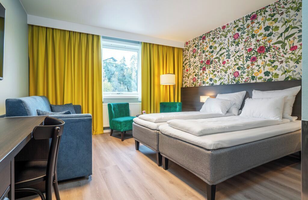 Una habitación de hotel con una cama, un escritorio, una silla y una ventana con cortinas.