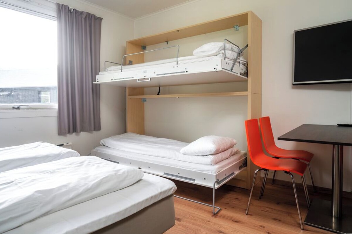 A room with two single beds, a bunk bed, a desk, a chair, and a TV.